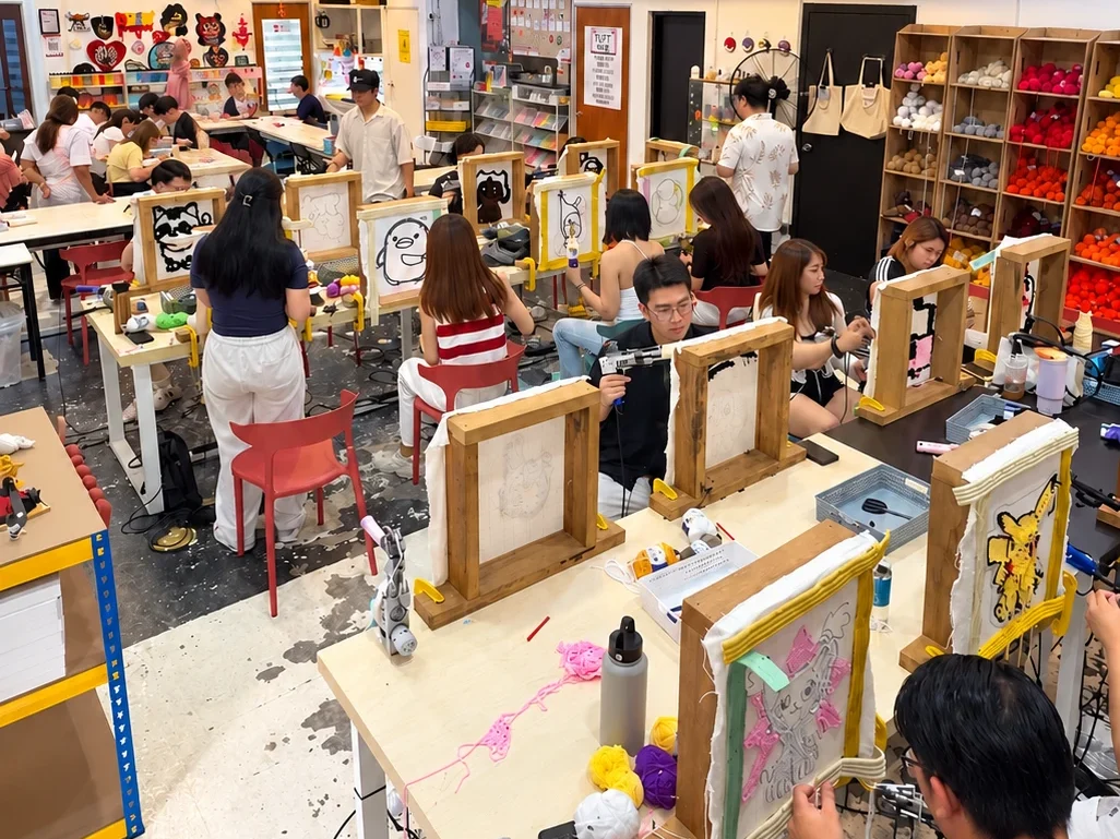 A full studio of people tufting rugs together at a party